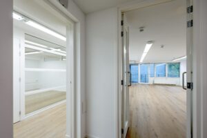 Doorkijk vanuit een gang naar twee moderne, lichte kantoorruimtes aan de Prins Hendrikkade met houten vloer en grote ramen.